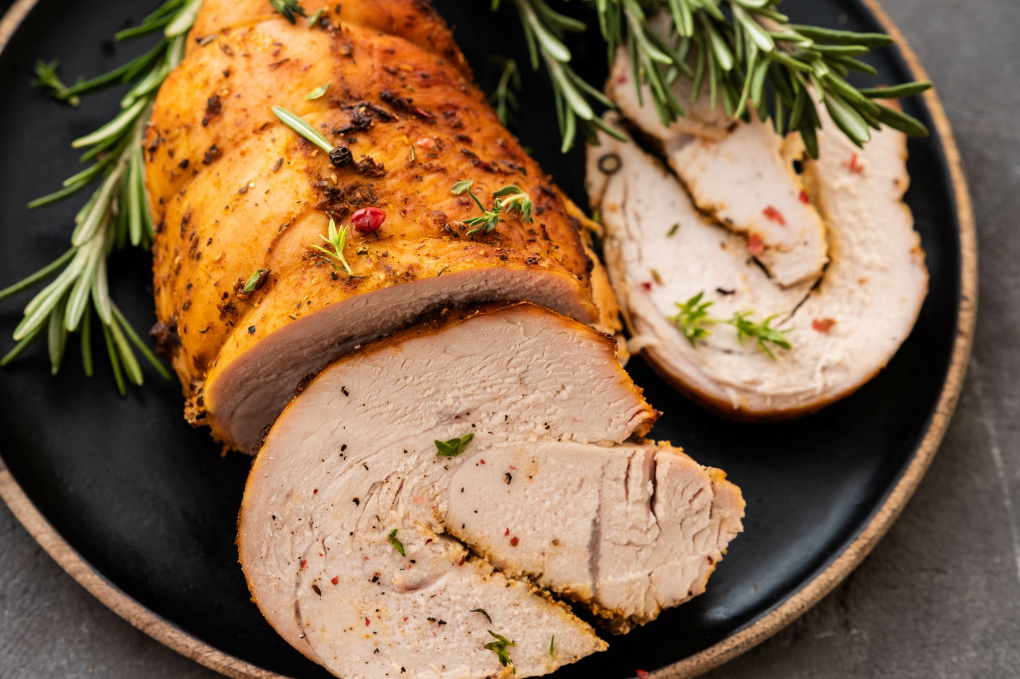 Stuffed turkey breast with baked vegetables and spices on a black background.