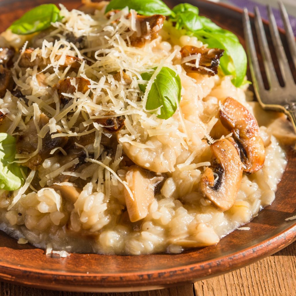 Italian dish - vegetarian mushroom risotto with basil leaves and Parmesan cheese in a clay plate naprostovatom village table